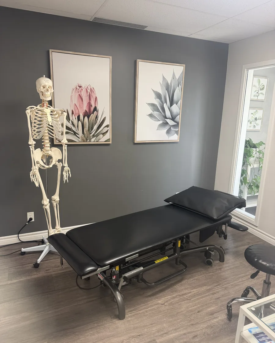 Treatment room with a black treatment table, an anatomical skeleton model and framed botanical prints